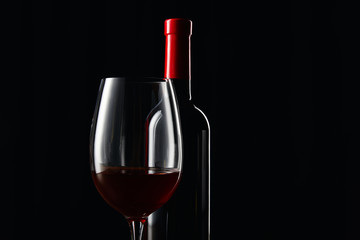 Bottle and glass of red wine isolated on black