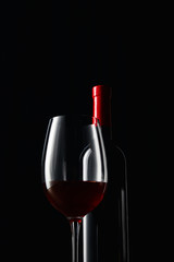 Bottle and glass of red wine isolated on black