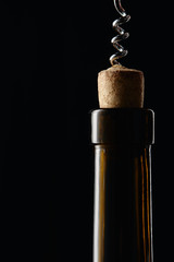 Glass wine bottle with wooden cork and corkscrew isolated on black