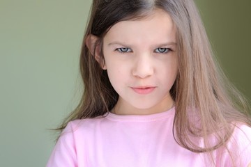 Green eyed caucasian white girl with fun angry face and long disheveled hair on blurred neutral background looking at the camera. Kid emotional portrait. Funny expression faces. 