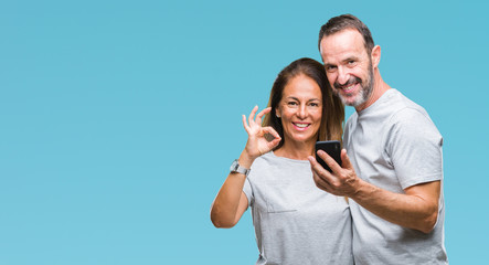Fototapeta premium Middle age hispanic couple texting message on smartphone ver isolated background doing ok sign with fingers, excellent symbol