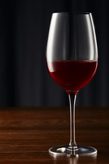 Wine glass with red wine on wooden surface on dark