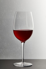 Wine glass with burgundy red wine on dark surface on grey