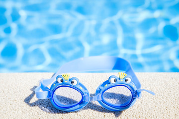 Closeup view of a boy blue swimming goggles on the pool edge with a big blue water copy space during a sunny summer day