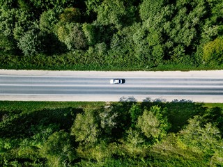 Aerial view of road with car going through green forest.