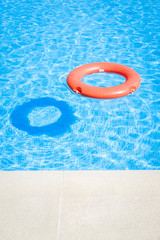 Closeup view of a red ring life buoy and its shadow floating on the blue water of the swimming pool during a sunny summer day