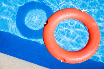 Closeup view of a red ring life buoy and its shadow floating on the blue water of the swimming pool...