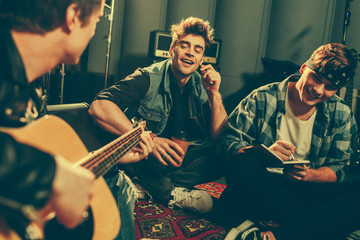 selective focus of cheerful friends looking at musician playing acoustic guitar