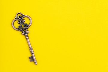 Rustic vintage bronze key on solid yellow background with copy space, key for business success, unlock or secret key for treasure