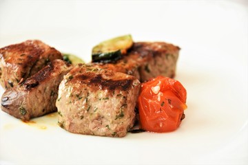 slice of roasted meat with zucchini and mini tomatoes on white background