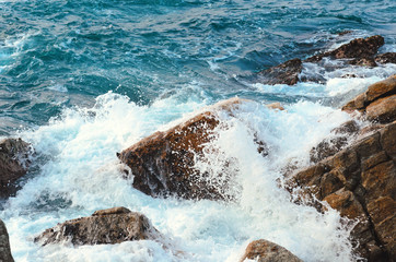 Stream of water crashes at rocky beach, raging sea. Sea water with foam, wave and beach. Nature wallpaper. Top view.  Photo with blur in motion..