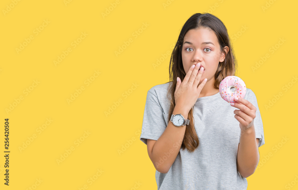 Sticker young beautiful woman eating pink donut over isolated background cover mouth with hand shocked with 