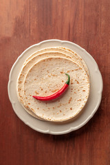 A chili pepper, shot from the top on a pile of tortillas, Mexican flatbreads, on a dark rustic wooden background with a place for text