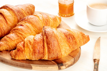 A high key closeup photo of a breakfast with croissants, coffee, and jam