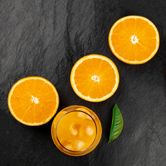 A glass of fresh orange juice with orange halves and a green leaf, shot from the top on a black background with a place for text