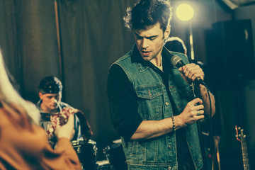 selective focus of handsome singer standing with microphone near rock band