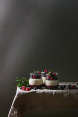 Homemade classic dessert Panna cotta with raspberry and blueberry berries and jelly in jars, decorated by mint leaves over linen table cloth with grey wall at background.