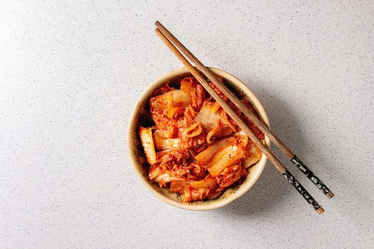 Korean traditional fermented appetizer kimchi cabbage salad in ceramic bowl with shopsticks over grey spotted background. Flat lay, space.
