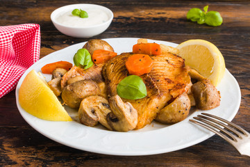 Tilapia fish fillet baked with vegetables, carrot, celery and mushrooms. White plate on wooden rustic table
