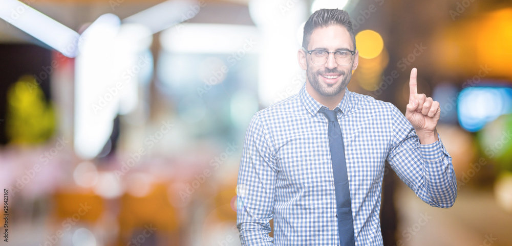 Wall mural Young business man wearing glasses over isolated background showing and pointing up with finger number one while smiling confident and happy.