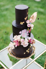 Closeup of black wedding cake with flowers. cake on the cake-shelf. Cake decorated with pink and purple flowers with gold details