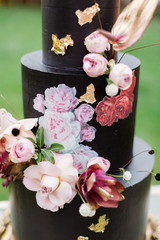 Closeup of black wedding cake with flowers. cake on the cake-shelf. Cake decorated with pink and purple flowers with gold details