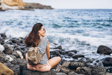 Fototapeta na wymiar Pretty long hair tourist girl relaxing on the stones near sea.