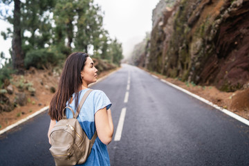 Rear view of long hair brunette girl walking on the foggy road in the mountains - Powered by Adobe