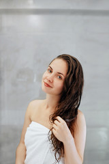 Hair  skin care concept. Beautiful young woman touching her wet  hair with hands and smiling while standing in front of the mirror  in bathroom. Care hair and skin