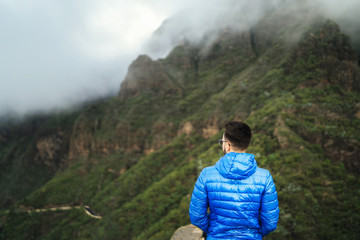 Man in blue jacket relaxing in the mountains with cloudy sky