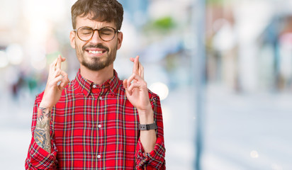 Young handsome man wearing glasses over isolated background smiling crossing fingers with hope and eyes closed. Luck and superstitious concept.