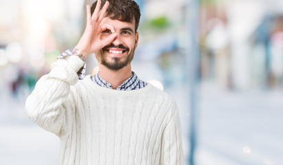 Young handsome man wearing winter sweater over isolated background doing ok gesture with hand smiling, eye looking through fingers with happy face.