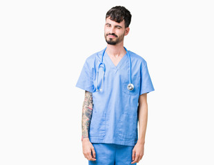 Young handsome nurse man wearing surgeon uniform over isolated background winking looking at the camera with sexy expression, cheerful and happy face.