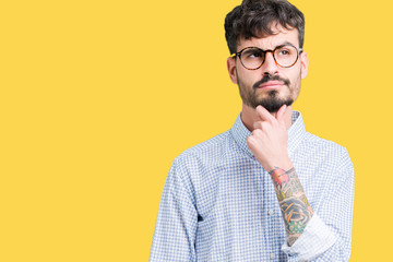 Young handsome man wearing glasses over isolated background with hand on chin thinking about question, pensive expression. Smiling with thoughtful face. Doubt concept.