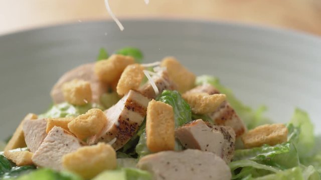 Camera follows shredding parmesan cheese over caesar salad. Shot with high speed camera, phantom flex 4K. Slow Motion.