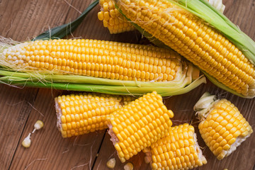 Fresh corn on cobs on rustic wooden table, closeup. Ripe corn. Half of broken open sweet corn