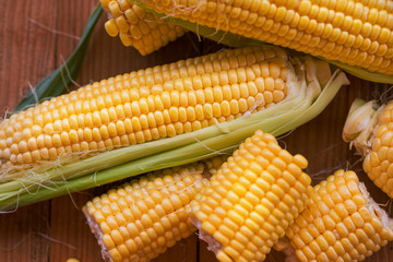 Fresh corn on cobs on rustic wooden table, closeup. Ripe corn. Half of broken open sweet corn