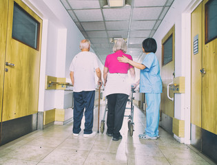 Asian nurse assisting aged senior woman with walker and man with stick in rehab facility