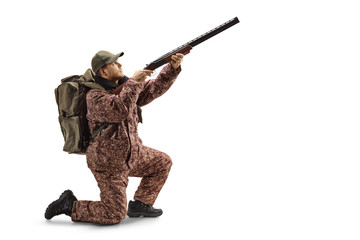 Man hunter in a uniform kneeling with a shotgun aiming up