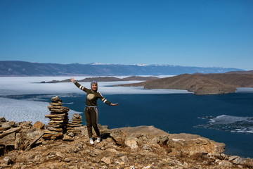 Fototapeta na wymiar View above big beautiful lake Baikal with Ice floes floating on the water and girl stands near rocks, Russia
