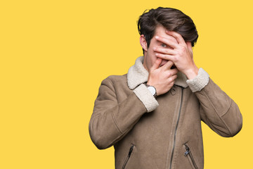 Young handsome man wearing winter coat over isolated background Covering eyes and mouth with hands, surprised and shocked. Hiding emotion