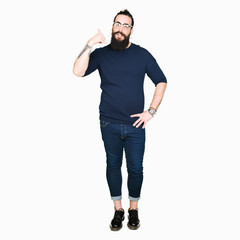 Fototapeta premium Young hipster man with long hair and beard wearing glasses smiling doing phone gesture with hand and fingers like talking on the telephone. Communicating concepts.