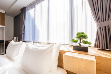Close-up of white pillow on bed decoration with light lamp and green tree in flowerpots in hotel bedroom interior.