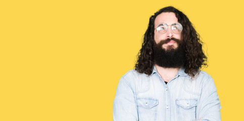 Obraz premium Young hipster man with long hair and beard wearing glasses smiling looking side and staring away thinking.