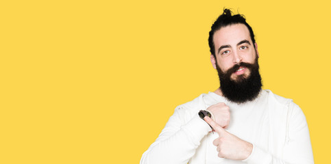 Young hipster man with long hair and beard wearing sporty sweatshirt In hurry pointing to watch time, impatience, upset and angry for deadline delay