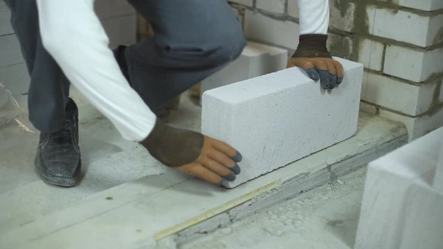 tilt up of builder laying first block according to mark on floor foundation