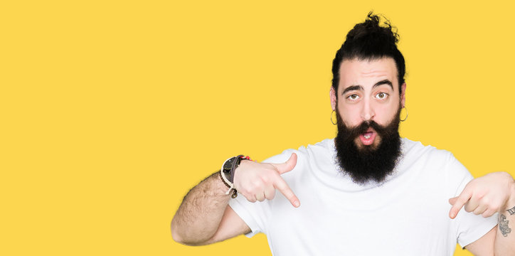 Young hipster man with long hair and beard wearing casual white t-shirt Pointing down with fingers showing advertisement, surprised face and open mouth