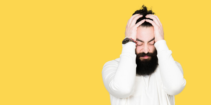Young man with long hair and beard wearing sporty sweatshirt suffering from headache desperate and stressed because pain and migraine. Hands on head.