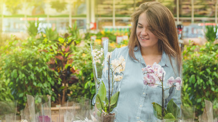 Beautiful female customer smelling colorful blooming orchids in the retail store. 