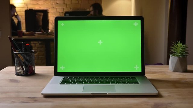 Closeup shoot of the laptop with green screen on the desk in the office indoors capturing the workplace organization
